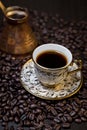 Selective focus shot of cup of coffee and cezve on spilled roasted coffee beans