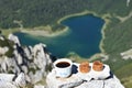 Selective focus shot of cup of coffee with two sweets on stones and a lake in the mountains Royalty Free Stock Photo