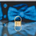 Selective focus shot of golden wedding rings on a mirror with a blue bow tie on a background Royalty Free Stock Photo