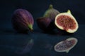 Selective focus shot of a half-sliced fig with a whole fig background on a blue surface