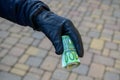 Selective focus shot of a hand wearing a leather glove holding a roll of euro banknotes