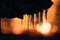 Selective focus shot of icicles hanging from a rock against a beautiful orange sunset