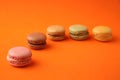 Selective focus shot of a pink macaron isolated on an orange surface with colorful macarons behind