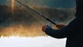 Selective focus shot of a silhouette of a fisherman holding the spinning reel of a fishing rod. Royalty Free Stock Photo