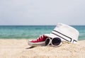 Selective focus shot of sunglasses, a white hat and red sneakers on a sandy beach Royalty Free Stock Photo