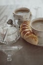 Selective focus shot of two cups of cappuccino with a homemade cheese roll and sugar on a table