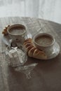 Selective focus shot of two cups of cappuccino with homemade cheese rolls and sugar on a table