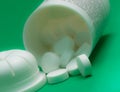 Selective focus shot of white round pills pouring out of the medicine bottle on green background Royalty Free Stock Photo