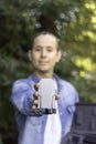 Selective focus of a small folded drone held by the hands of a young man dressed in denim clothes in the woods
