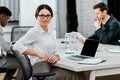 Selective focus of smiling businesswoman in eyeglasses looking at camera in office Royalty Free Stock Photo