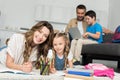 selective focus of smiling mother and daughter doing homework while father and son using laptop on sofa Royalty Free Stock Photo