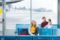 Selective focus of smiling woman sitting in airport near backpack with people