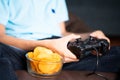 Selective focus on snacks, kid playing video game and placing chips to eat at while playing at home during leisure time Royalty Free Stock Photo