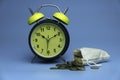 Selective focus of table clock and a rug sack full with a gold coins isolated on a blue background. Business and finance concept Royalty Free Stock Photo