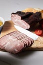 Focus of tasty ham on cutting board with knife, cherry tomato and baguette on white surface