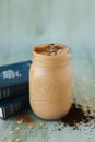 Selective focus of a thick chocolate milkshake in the glass jar next to books on a blurry background