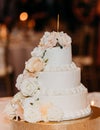 Selective focus of the three-tiered wedding cake covered by white roses on the sparkling cake stand