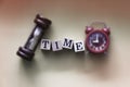 In selective focus of TIME word written on wood block put at the middle of blurred sandclock and red alarm clock