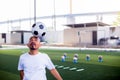 Selective focus to ball on head of football coach to demo for football player with blurry marker cones and soccer equipment Royalty Free Stock Photo