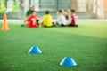 Selective focus to blue marker cones are soccer training equipment on green artificial turf with blurry kid players training backg Royalty Free Stock Photo