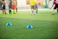 Selective focus to blue marker cones are soccer training equipment on green artificial turf with blurry kid players training backg Royalty Free Stock Photo
