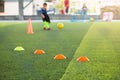 Selective focus to marker cones are soccer training equipment on green artificial turf with blurry kid players training background Royalty Free Stock Photo