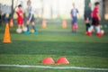 Selective focus to red marker cones are soccer training equipment on green artificial turf with blurry kid players training Royalty Free Stock Photo