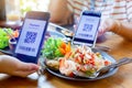 Selective focus to smartphone in hand to scan QR code on tag with blurry spicy Thai food
