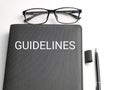 Selective focus top view text GUIDELINES on black book with pen and eye glasses isolated on white background. Royalty Free Stock Photo