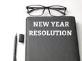 Selective focus top view text NEW YEAR RESOLUTION on black book with pen and eye glasses isolated on white background. Royalty Free Stock Photo