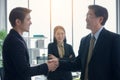 Two Asian young and senior businessmen are shaking hands and smiling in foreground and blur businesswoman in background