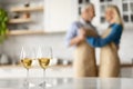 Selective focus on two glasses of white wine on kitchen table over dancing senior couple Royalty Free Stock Photo