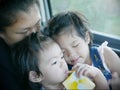 Two little Asian baby girls, siblings, cuddling on her mother`s lap in a car during a trip Royalty Free Stock Photo