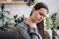 Selective focus of unhealthy young woman having neck pain sitting on couch at home. Upset girl has pain from muscles. Cervical