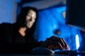 Selective focus of unrecognizable hooded hacker man wearing anonymous mask using laptop and desktop computer to hack