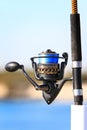 Selective focus vertical shot of a blue and black fishing rod on a pier waiting for a bite