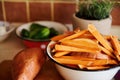 Focus on wedges of organic sweet potato in an enamel vintage bowl next to tubers of batata against a pot with rosemary