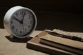 Table clock and ballpoint pen on stack notebooks with sunlight and shadow on wooden table surface