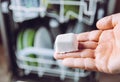 Selective focus on woman hand, holding homemade natural dishwasher pod defocus dishes in dishwasher on background.