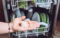 Selective focus on woman hand, holding homemade natural dishwasher pod defocus dishes in dishwasher on background.