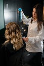 Selective focus on woman with long curling hair in hair salon, hairdresser with hairspray at background