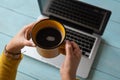 Selective focus of woman`s hands holding a cup with coffee on a laptop. Royalty Free Stock Photo