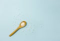 Selective focus on wooden spoon with small white round homeopathy pills against blue background.