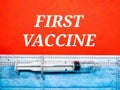 Selective focus. Word FIRST VACCINE with syringe and face mask on red background.Shot were noise and film grain.