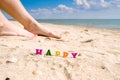 Selective focus on the word Happy on the background of female feet and the sea. Royalty Free Stock Photo