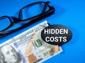 Selective focus.Word HIDDEN COSTS with glasses and dollar banknote on blue background.Business concept. Royalty Free Stock Photo