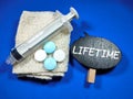 Word LIFETIME on wooden board with syringe and medicine on blue background.