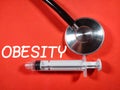 Selective focus.Word OBESITY with syringe and stethoscope on red background.Medical concept.