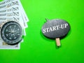 Selective focus.Word start up on wooden board with compass and banknote on a green background.Shot were noise and film grain.