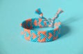 Selective focus of woven friendship bracelet, handmade of thread and knots, with blue, pink hearts pattern. On blue background